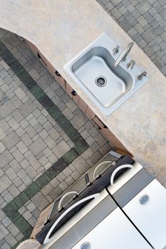 Upmarket outdoor kitchen and large built in gas barbecue in a corner design with a decorative cement counter top and sink, overhead view on a brick patio