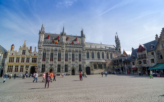 Bruges, Belgium - May 11, 2015: Tourist on Burg square with City Hall and Basilica of the Holy Blood in Bruges, Belgium on May 11, 2015. The historic city centre is a prominent World Heritage Site of UNESCO.