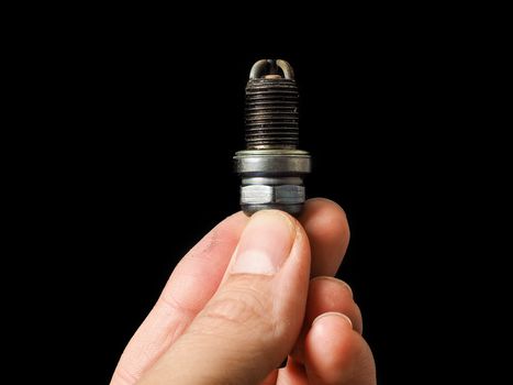 Hand of a male person holding a worn spark plug isolated on black