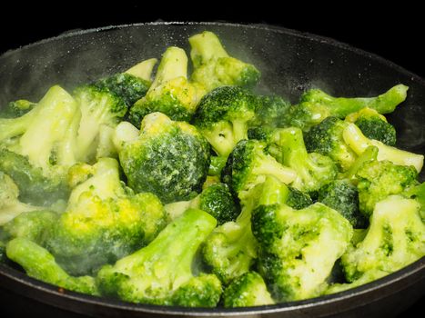 Thawing frozen green broccoli in a hot fry pan