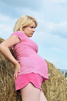 pensive pregnant woman stending near the haystack