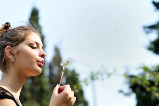 teen pretty girl blowing on dandelion outdoors 