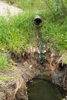 Concrete circular run-off pipe in the green grass discharging water