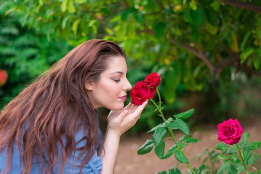 Young beautiful Caucasian girl smelling the roses in the garden.