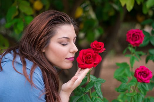 Young beautiful Caucasian girl smelling the roses in the garden.