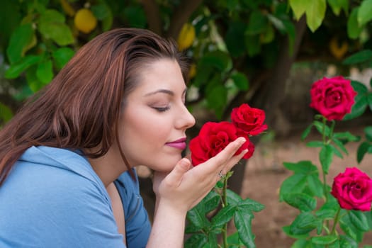 Young beautiful Caucasian girl smelling the roses in the garden.