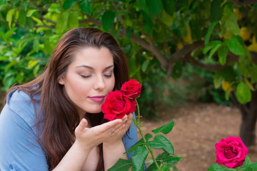 Young beautiful Caucasian girl smelling the roses in the garden.