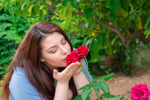 Young beautiful Caucasian girl smelling the roses in the garden.