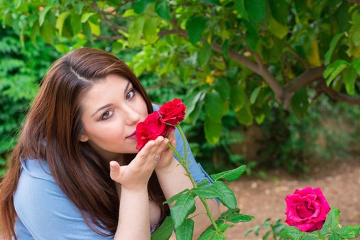 Young beautiful Caucasian girl smelling the roses in the garden.