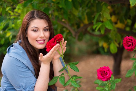 Young beautiful caucasian girl holding red roses in the garden, smiling.