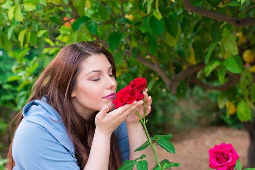 Young beautiful Caucasian girl smelling the roses in the garden.