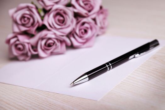 blank card with a pen and  purple roses 