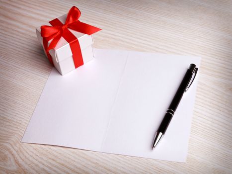 Blank card, pen and white gift box with red ribbon