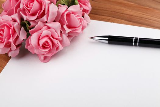 blank sheet of paper with a pen and pink roses