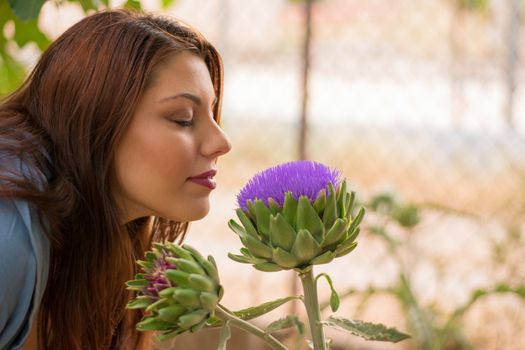 Young beautiful caucasian girl smelling a big artichoke flower.