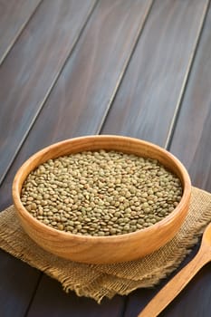 Raw lentils (lat. Lens culinaris) in wooden bowl, photographed on dark wood with natural light (Selective Focus, Focus one third into the lentils)