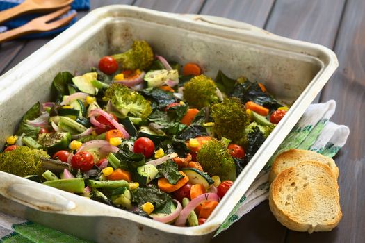 Baked vegetables (zucchini, onion, cherry tomato, broccoli, carrot, sweet corn, green bean, chard) seasoned with thyme in baking dish, photographed with natural light (Selective Focus, Focus one third into the image)