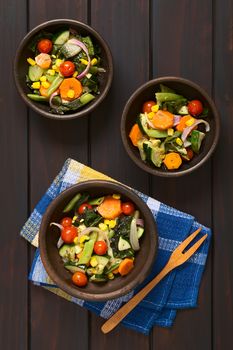 Overhead shot of three rustic bowls of baked vegetables (zucchini, onion, cherry tomato, broccoli, carrot, sweet corn, green bean, chard) seasoned with thyme, photographed on dark wood with natural light