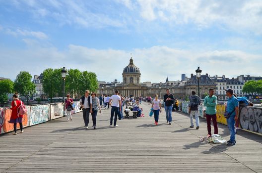 Paris, France - May 13, 2015: People visit Institut de France and the Pont des Arts or Passerelle des Arts bridge across river Seine in Paris, France. on May 13, 2015.