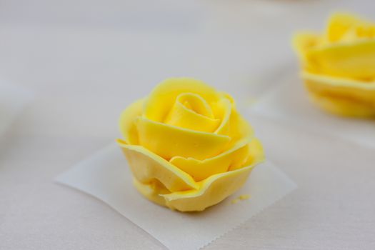 Yellow roses made from butter cream icing, drying on parchment paper.
