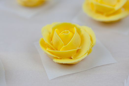 Yellow roses made from butter cream icing, drying on parchment paper.