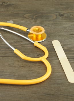 Wooden tongue depressor and stethoscope placed on table in examination room.                                 