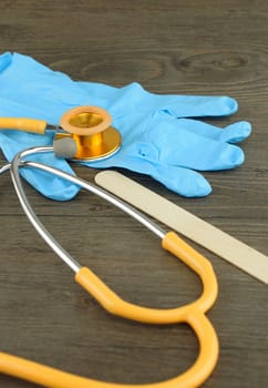 Medical examination such as stethoscope, wooden tongue depressor and glove placed on table.                     