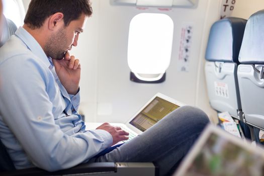 Casually dressed middle aged man working on laptop in aircraft cabin during his business travel. Shallow depth of field photo with focus on businessman eye.