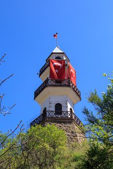 Buttom view of wooden tower building with Turkish flag waving, under blue sky.