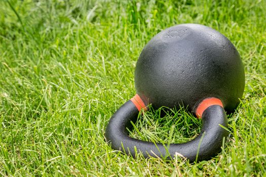 heavy iron competition kettlebell (62lb - 28 kg) on green grass in backyard - outdoor fitness concept