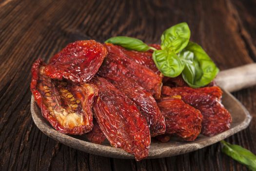 Sundried tomatoes and fresh basil leaves on brown wooden background. Culinary italian eating. 