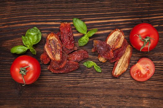 Delicious sundried and fresh tomatoes on brown wooden vintage textured background, top view. Traditional mediterranean kitchen.