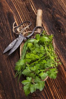 Various aromatic culinary herbs. Thyme, marjoram, basil, mint, chives and parsley on wooden plate on old brown wooden background. Rustic, vintage, natural, country style images.