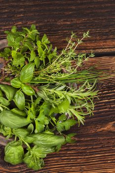 Various aromatic culinary herbs. Fresh thyme, marjoram, basil, mint, chives and parsley herbs on plate on old brown wooden background, top view. Rustic, vintage, natural, country style images.