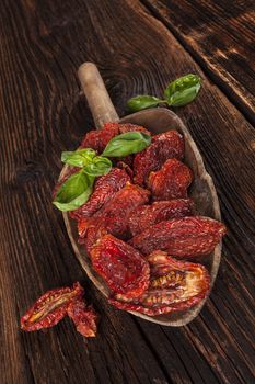 Sundried tomatoes and fresh basil leaves on brown wooden background. Culinary italian eating. 