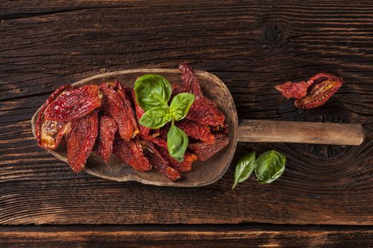 Sundried tomatoes and fresh basil leaves on brown wooden background. Culinary italian eating. 