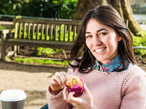 Beautiful Woman Having a Muffin Outside at the Coffee Shop and Looking at Camera with a Smile