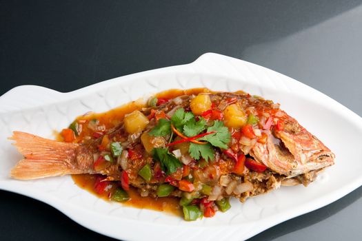 Freshly prepared Thai style whole fish red snapper dinner with tamarind sauce on a white fish shaped plate. Shallow depth of field.