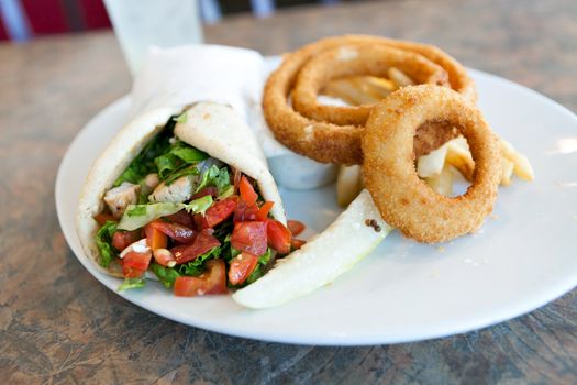 Chicken pita wrap sandwich with onion rings and a deli pickle slice. Shallow depth of field.