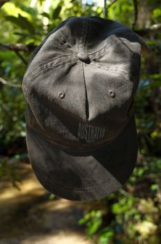 An Australia cap hanging from a tree branch on a padded clothes hanger near a waterfall