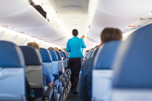 Interior of airplane with passengers on seats and stewardess walking the aisle, closing the overhead luggage bins.