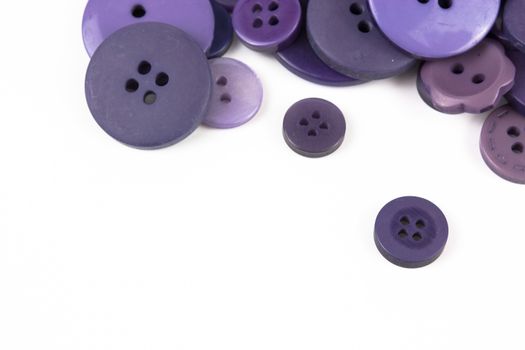 Close up of various purple button scattered on a white surface.
