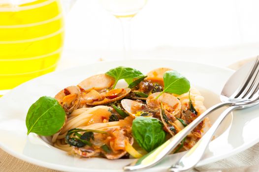 A white plate with delicious spaghetti shellfish and green basil. A glass of white wine in background.