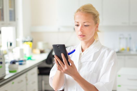 Portrait of an attractive, young, confident female health care professional in his working environment making notes on her smarth phone.