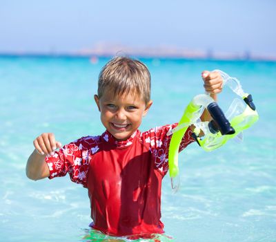 Portrait of happy cute boy with snorkeling mask ready to dive in the sea