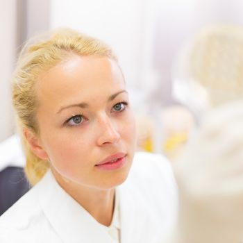 Female life science professional observing cell culture samples on LB agar medium in petri dish.  Scientist grafting bacteria in microbiological analytical laboratory .  Focus on scientist's eye.