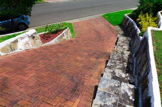 A car parked on the street in front of a neat suburban driveway with lawn and plantings in a Sydney Australia suburb,