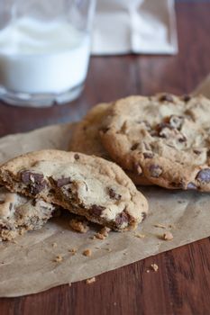 Fresh chocolate chunk cookies on a piece of brown paper  with a glass of miolk on a wooden table.