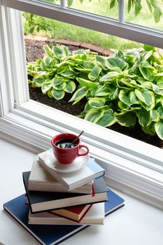 Cup of Hot Coffee on Top of Piled Books Next to Open Glass Window For Reading Time Concept.