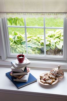Cup of Hot Black Coffee on Piled Books and Plate of Tasty Puff Pastries at the Glass Window for Reading Time with Snacks Concept.
